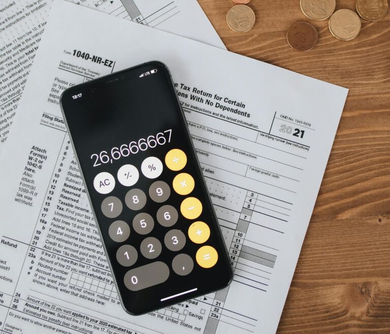 Calculator displaying number placed on tax forms with scattered coins on wooden desk.